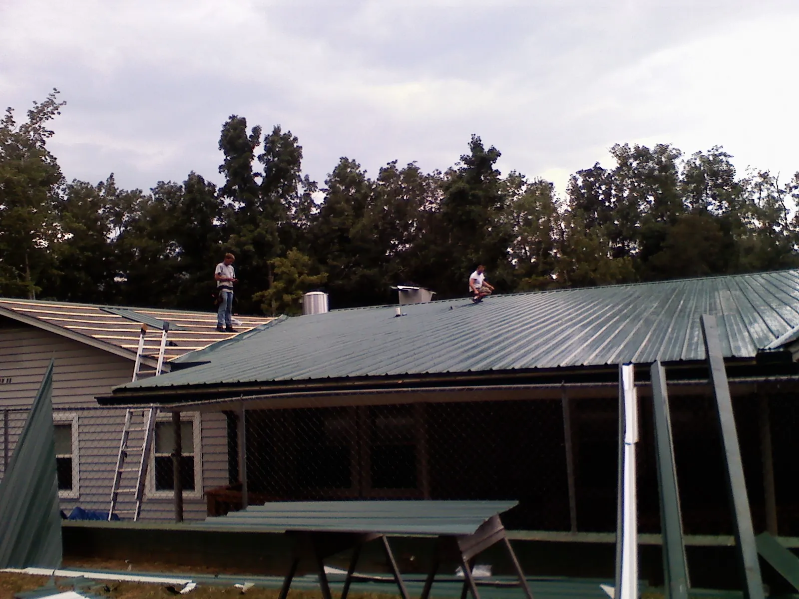 Two roofers installing green metal panels above a covered porch in Martinsburg